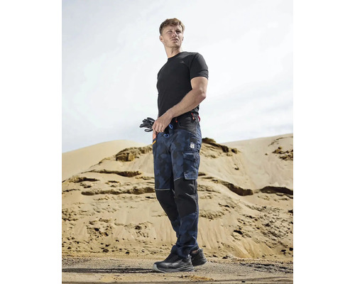 Muž v pracovnom odeve s pracovnými nohavicami, tričkom a bezpečnostnou obuvou pred piesočným kopcom