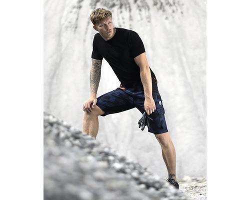 Muž má na sebe krátke pracovné nohavice s maskovacím vzorom, tričko a rukavice