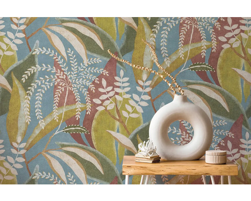 Vliesová tapeta s veľkým vzorom listov v modrej, zelenej a hnedej farbe za dreveným stolíkom s okrúhlou bielou vázou.