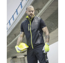 Muž má na sebe pracovnú vestu, tričko, pracovné nohavice, rukavice a drží ochrannú prilbu.