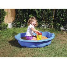 Dievča sa hrá v záhrade v modrom pieskovisku s hračkami do piesku.