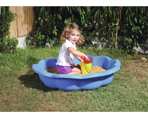 Dievča sa hrá v záhrade v modrom pieskovisku s hračkami do piesku.