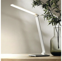 Biela LED stolná lampa na stole, vedľa vázy s rastlinami