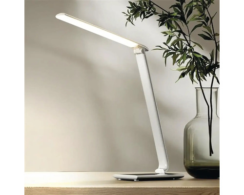 Biela LED stolná lampa na stole, vedľa vázy s rastlinami