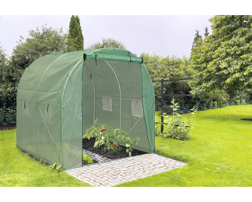 Zelený fóliový skleník s otvorenými dverami na dláždenej ploche v záhrade.