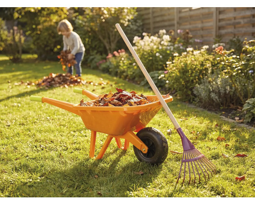 Záhradná scéna s fúrikom, hrabľami a dieťaťom zbierajúcim lístie