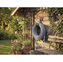 Záhradná scéna s navijakom hadice na drevenej stene, obklopená rastlinami