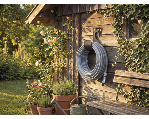 Záhradná scéna s navijakom hadice na drevenej stene, obklopená rastlinami