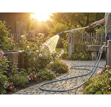 Osoba zavlažuje ruže záhradnou hadicou na dláždenej ceste.