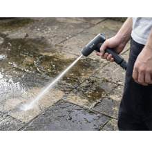 Osoba čistí kamenné dosky vonku pomocou akumulátorovej vysokotlakovej umývačky.