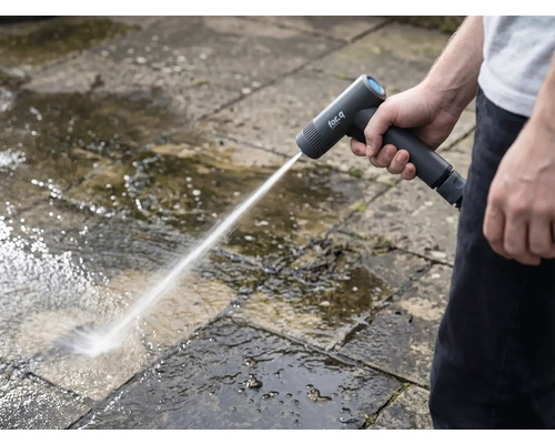Osoba čistí kamenné dosky vonku pomocou akumulátorovej vysokotlakovej umývačky.