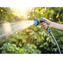 Ruka drží záhradnú hadicu so sprchovou hlavicou pri zavlažovaní