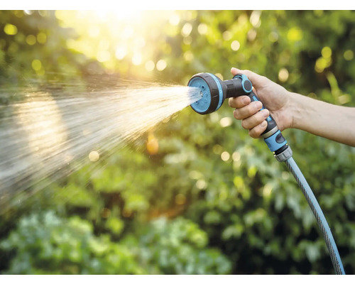 Ruka drží záhradnú hadicu so sprchovou hlavicou pri zavlažovaní