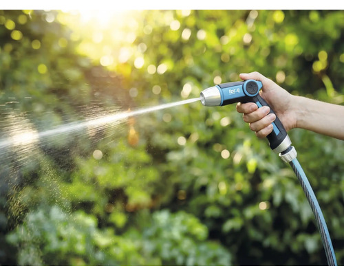 Ruka drží záhradnú striekaciu pištoľ for_q, z ktorej tryská prúd vody.