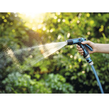 Osoba drží záhradný postrekovač a zalieva rastliny.