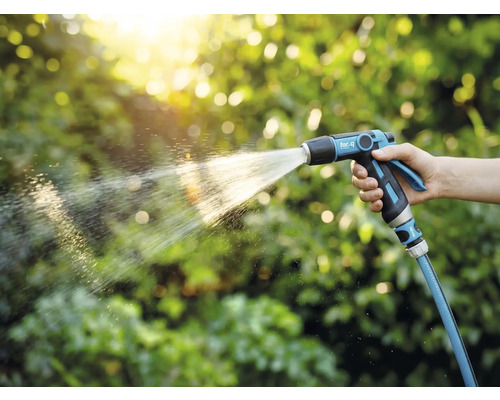 Osoba drží záhradný postrekovač a zalieva rastliny.