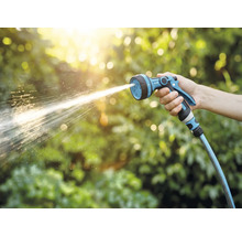 Ruka drží záhradný postrekovač, z ktorého strieka voda