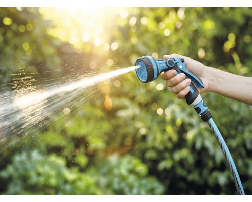 Ruka drží záhradný postrekovač, z ktorého strieka voda