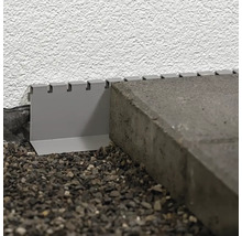 Detail kovového okraja trávnika medzi dlažobnými kockami a stenou.