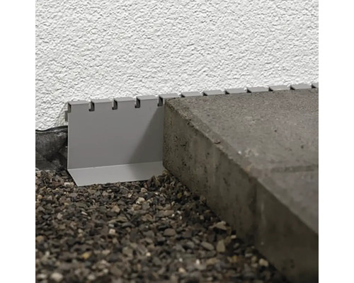 Detail kovového okraja trávnika medzi dlažobnými kockami a stenou.