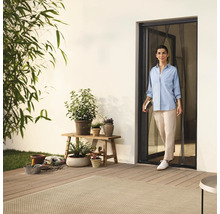 Žena vstupuje na terasu dverami so sieťou proti hmyzu, obklopená rastlinami a záhradným príslušenstvom.