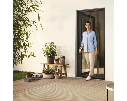 Žena vstupuje na terasu dverami so sieťou proti hmyzu, obklopená rastlinami a záhradným príslušenstvom.