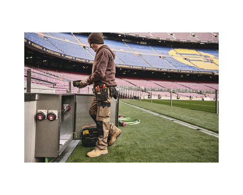 Muž s opaskom na náradie a pracovným odevom pracujúci na elektrickej skrini na štadióne.