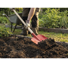 Osoba rýľuje zeminu v záhrade rýľom. V pozadí je fúrik.