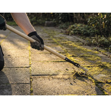 Osoba odstraňuje mach medzi dlažobnými kockami pomocou čističa škár.