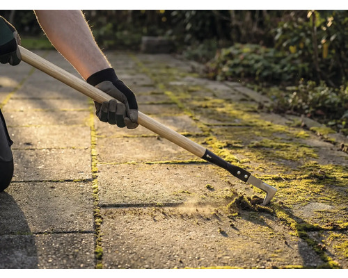 Osoba odstraňuje mach medzi dlažobnými kockami pomocou čističa škár.