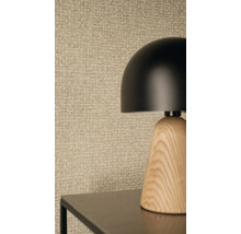 Moderná stolná lampa s čiernym kopulovitým tienidlom a dreveným podstavcom pred štruktúrovanou tapetou s tkaným vzorom.