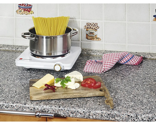 Scéna kuchyne s varnou doskou, cestovinami, syrom a paradajkami na pracovnej doske.