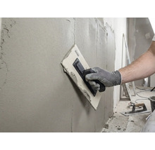 Remeselník hladí stenu pomocou hladidla a tmelu.