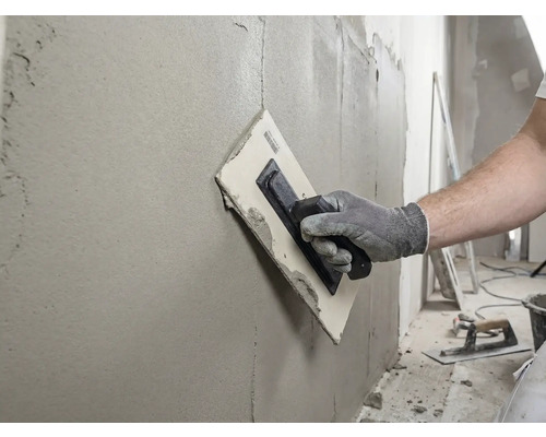 Remeselník hladí stenu pomocou hladidla a tmelu.