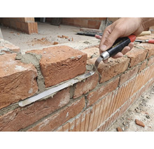 Remeselník pracuje s tehlovou stenou s škárovacou lyžicou