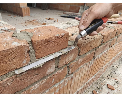 Remeselník pracuje s tehlovou stenou s škárovacou lyžicou