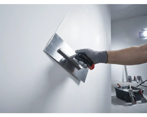 Ruka so stierkou na sadru pri vyhladzovaní steny