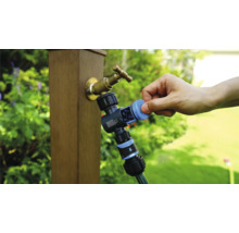 Záhradný kohútik s rozdeľovačom vody a pripojenou záhradnou hadicou počas používania.