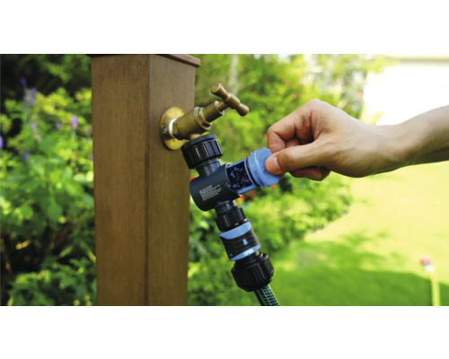 Záhradný kohútik s rozdeľovačom vody a pripojenou záhradnou hadicou počas používania.