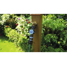 Záhradná scéna s vodovodným kohútikom na drevenom stĺpiku a pripojenou záhradnou hadicou