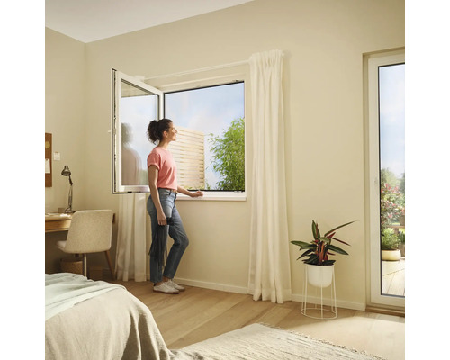 Svetlá spálňa s výklopným oknom a ženou, ktorá sa pozerá von