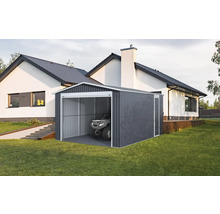Moderná plechová garáž v tmavosivej farbe s bielym rámom a štvorkolkou vo vnútri, na trávniku vedľa bieleho domu.