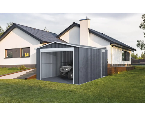 Moderná plechová garáž v tmavosivej farbe s bielym rámom a štvorkolkou vo vnútri, na trávniku vedľa bieleho domu.