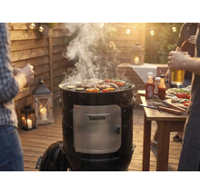 Údiaci gril s mäsom a zeleninou na grilovacej mriežke na záhradnej grilovačke.