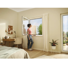 Svetlá izba s otvoreným oknom, písacím stolom, posteľou a ženou, ktorá sa pozerá z okna