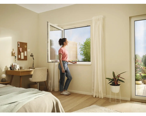 Svetlá izba s otvoreným oknom, písacím stolom, posteľou a ženou, ktorá sa pozerá z okna