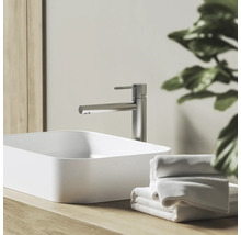 Moderná kúpeľňa s vysokou pákovou batériou z brúseného kovu a bielym obdĺžnikovým umývadlom na drevenej doske s uterákmi.