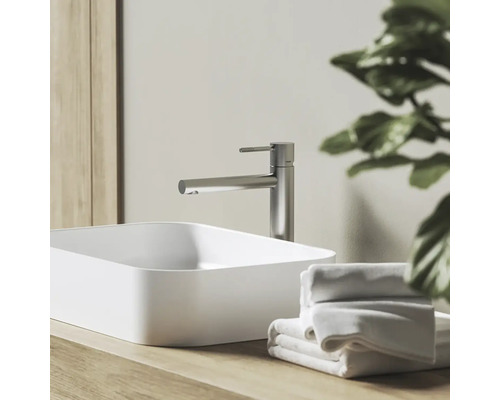 Moderná kúpeľňa s vysokou pákovou batériou z brúseného kovu a bielym obdĺžnikovým umývadlom na drevenej doske s uterákmi.