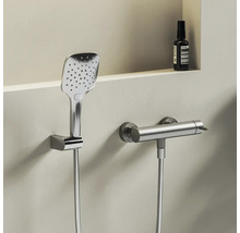 Moderná štvorcová ručná sprcha a valcová termostatická sprchová batéria z kovu na svetlej stene.