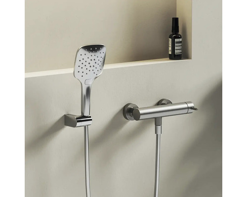 Moderná štvorcová ručná sprcha a valcová termostatická sprchová batéria z kovu na svetlej stene.